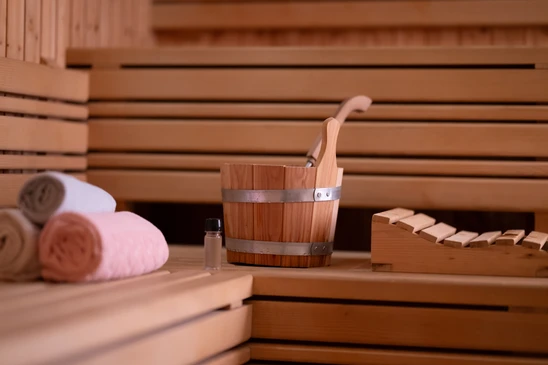 Sauna finlandais en bois clair avec banquettes étagées et vapeur s'échappant du poêle